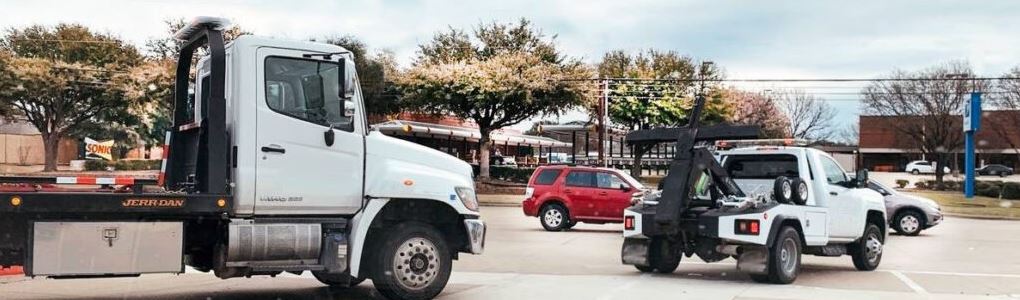 Two white tow trucks, a flatbed and a wrecker, on a city street